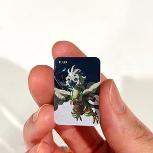 May include: A small rectangular card featuring a colorful illustration of the character Tulin, a bird-like creature with white feathers, green accents, and a bow. The background transitions from dark blue at the top to a white base with gray circular patterns.