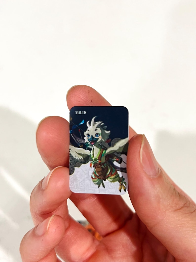 May include: A small rectangular card featuring a colorful illustration of the character Tulin, a bird-like creature with white feathers, green accents, and a bow. The background transitions from dark blue at the top to a white base with gray circular patterns.