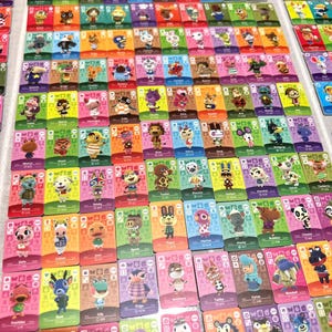 May include: A large collection of rectangular Animal Crossing trading cards arranged in a grid. Each card features a unique illustrated character, a coloured background, and various game-related icons including numbers and symbols.