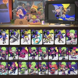 May include: A collection of colorful trading cards featuring characters from a video game. The cards have a vibrant design with ink splatters and character illustrations. The image also includes figurines and a retro television displaying game characters.