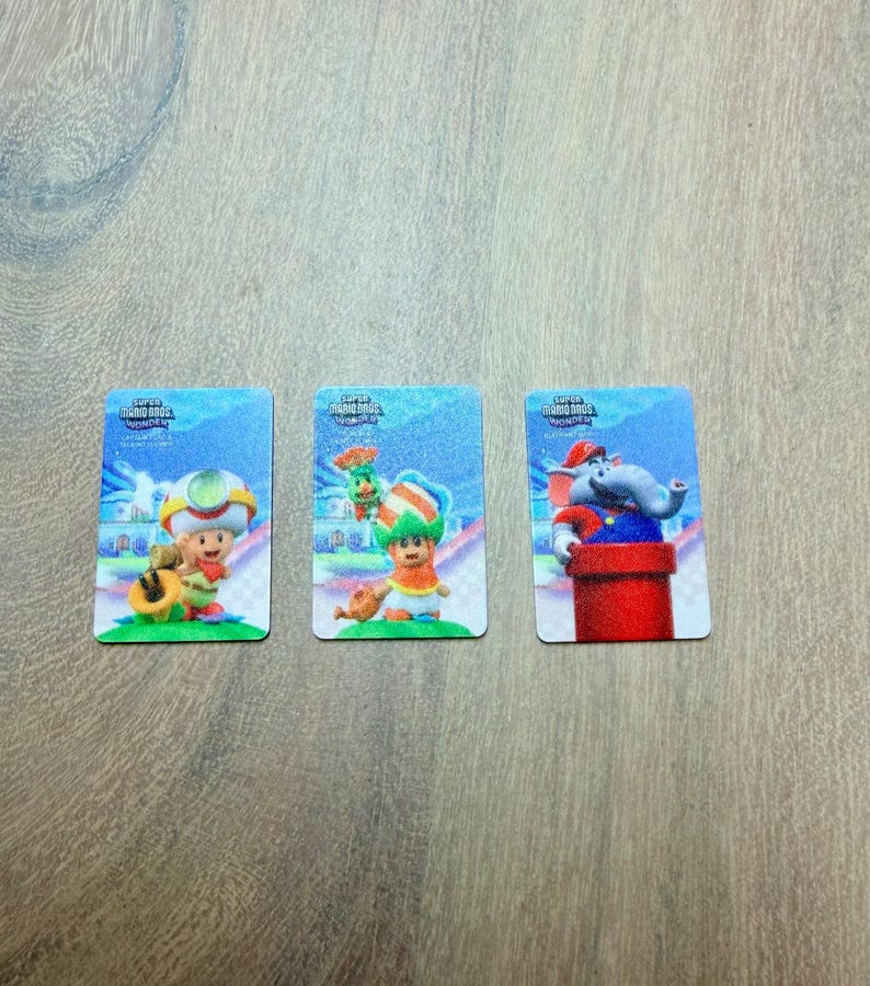 Puede incluir: Tres tarjetas rectangulares con personajes de Super Mario Bros. Wonder. Cada tarjeta tiene un fondo azul con una ilustraci&oacute;n de personaje. Los personajes incluyen Toad, un personaje con un sombrero verde y naranja y un personaje de elefante.