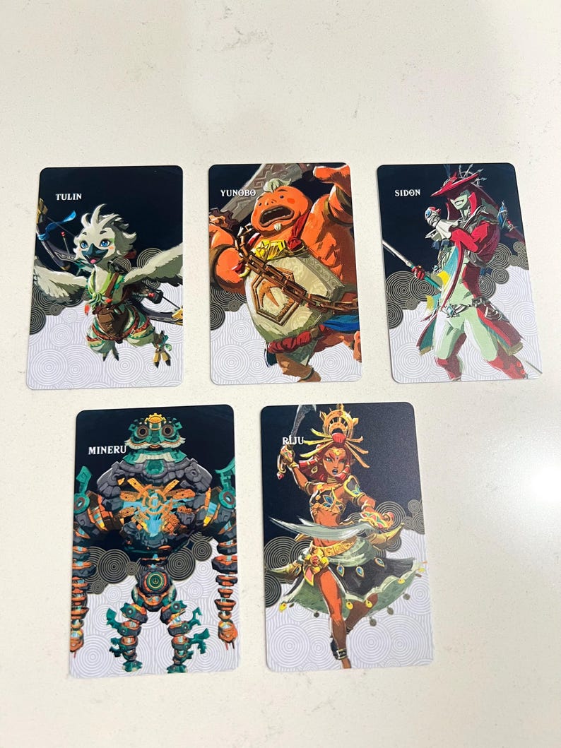 May include: Five rectangular trading cards featuring illustrated characters. The cards are labeled Tulin, Yunobo, Sidon, Mineru, and Riju. Each card displays a unique character in a dynamic pose against a black and white patterned background.