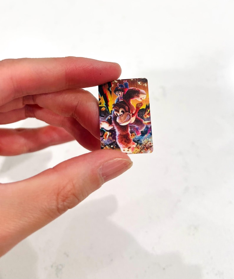 May include: A small, rectangular image with a colourful illustration of a cartoon ape character with a smaller figure riding on its back. The image has a vibrant, detailed design with a mix of warm and cool colours.