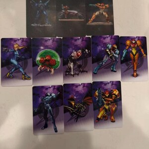 May include: A collection of rectangular trading cards featuring various characters and scenes from a science fiction video game. The cards display colorful illustrations of armored figures, creatures, and futuristic vehicles against a purple and black space-themed background.