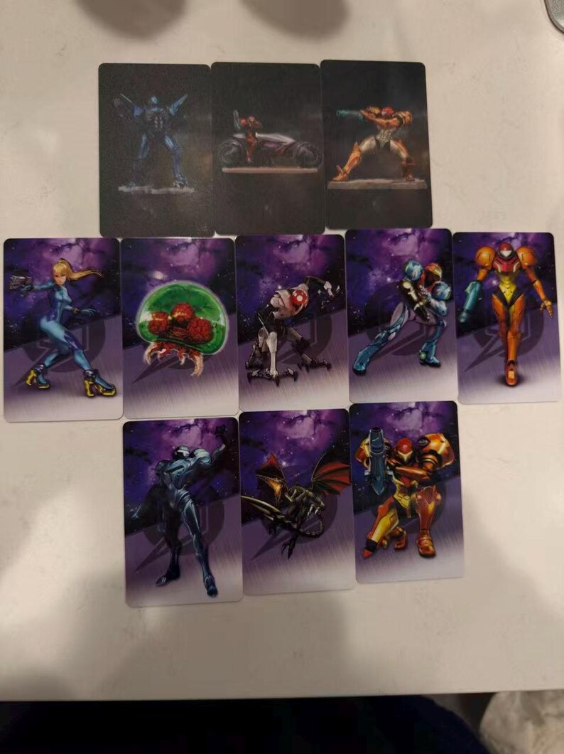 May include: A collection of rectangular trading cards featuring various characters and scenes from a science fiction video game. The cards display colorful illustrations of armored figures, creatures, and futuristic vehicles against a purple and black space-themed background.