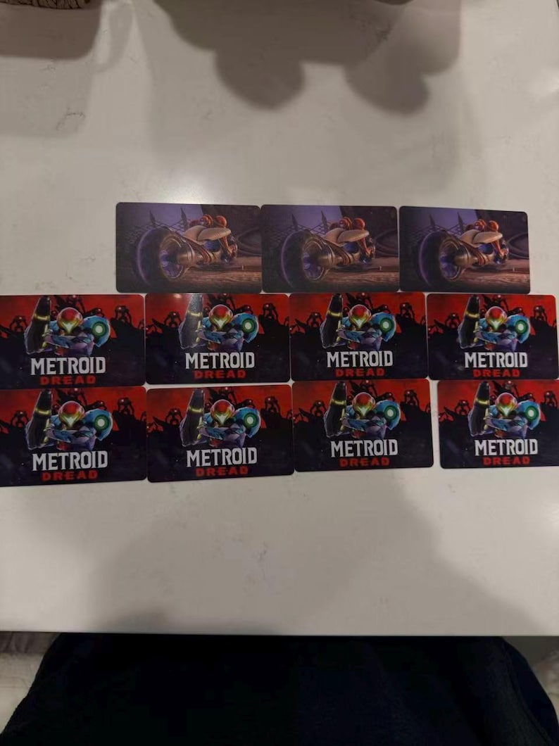 May include: A collection of rectangular cards featuring artwork from the video game Metroid Dread. The cards display images of a character in a suit and a vehicle, with the game's title prominently displayed.