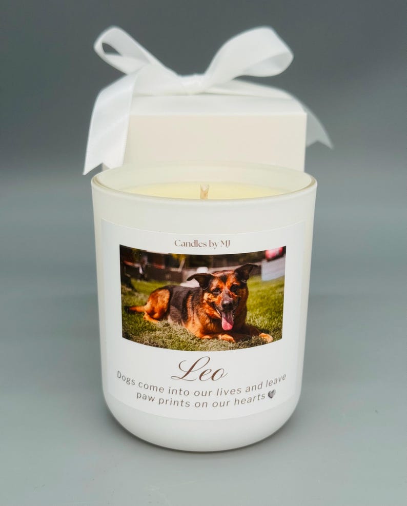 May include: White candle with a photo of a German Shepherd dog on the front. The candle has the text "Candles by MJ" and "Leo" on the front. The text below the photo reads "Dogs come into our lives and leave paw prints on our hearts".
