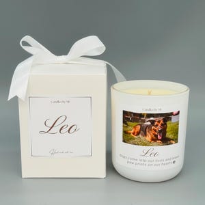 May include: White candle with a photo of a German Shepherd dog on the front. The candle has the words "Candles by Mi" and "Leo" printed on it. The text below the photo reads "Dogs come into our lives and leave paw prints on our hearts".