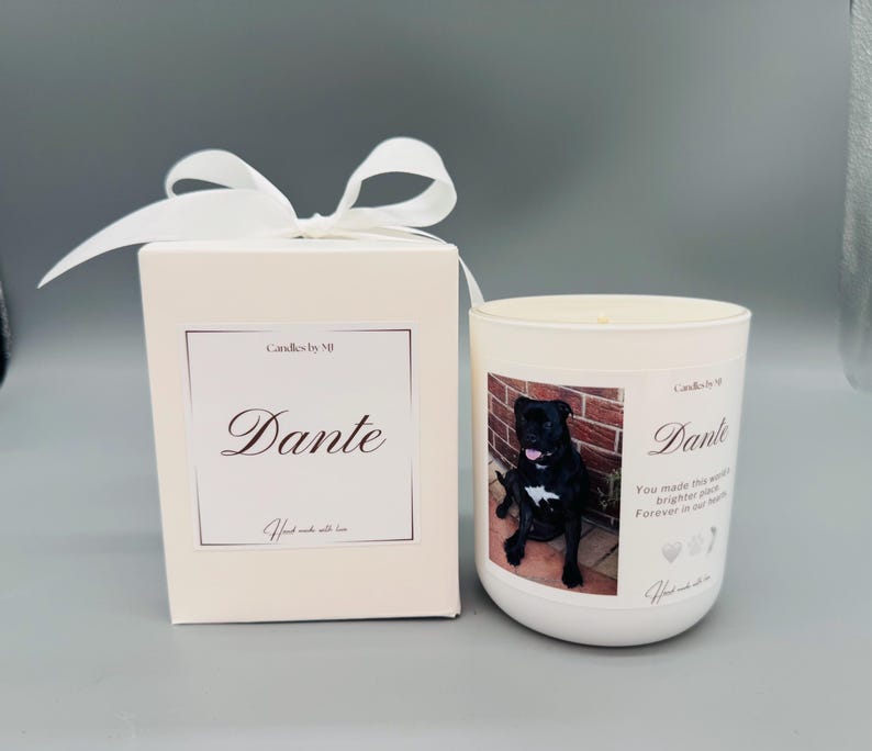 May include: White candle with a black and white photo of a dog on the front. The candle is in a white jar with a white label that says "Candles by MJ" and "Dante". The label also includes the text "You made this world brighter, our hearts forever in your paws".