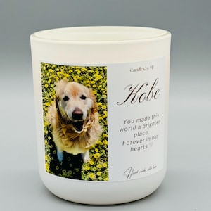 May include: White candle with a photo of a golden retriever in a field of yellow flowers. The text "Candles by M" and "Kobe" are printed on the candle. The text "You made this world a brighter place. Forever in our hearts" is also printed on the candle.