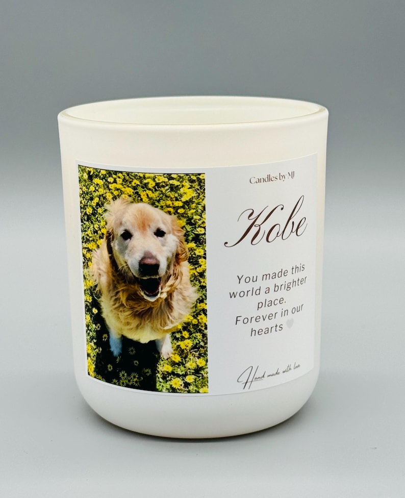 May include: White candle with a photo of a golden retriever in a field of yellow flowers. The text "Candles by M" and "Kobe" are printed on the candle. The text "You made this world a brighter place. Forever in our hearts" is also printed on the candle.