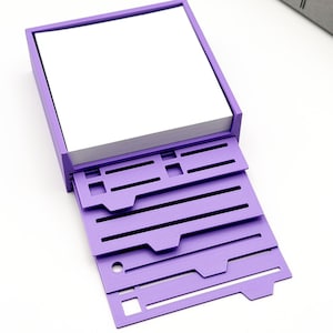 May include: A purple desk organizer with a stack of white paper inside. The organizer has several pull-out trays with cut-out designs. The design is a modern, minimalist style, perfect for office or home use.
