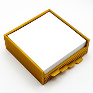 May include: Mustard yellow square notepad holder with a stack of white notepaper. The holder has a rectangular frame and four built-in tabs. The tabs are used to separate the notepaper. The notepad holder is made of plastic.