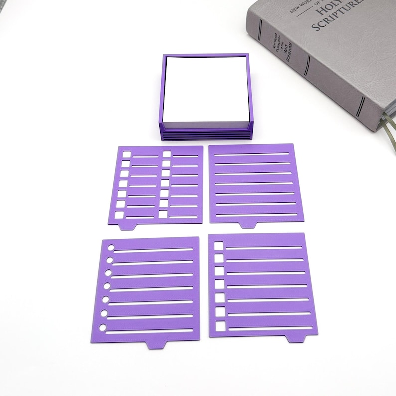 May include: A purple desk organizer set with a square notepad and four matching purple templates. The templates have different designs, including lined and checklist styles. A gray book is visible in the background.