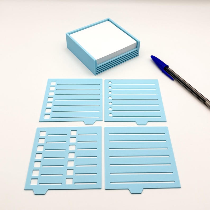 May include: A light blue desk organizer with a stack of white notepaper. Four light blue stencils with lined and dotted designs are arranged below the organizer. A blue and black pen rests on the surface.