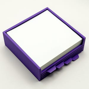 May include: A square, purple desk organizer with a stack of white notepaper. The organizer has a rectangular frame and a series of tabs on one side. The tabs are designed to help organize the notepaper.