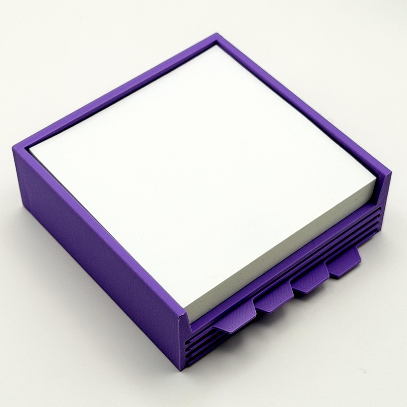 May include: A square, purple desk organizer with a stack of white notepaper. The organizer has a rectangular frame and a series of tabs on one side. The tabs are designed to help organize the notepaper.