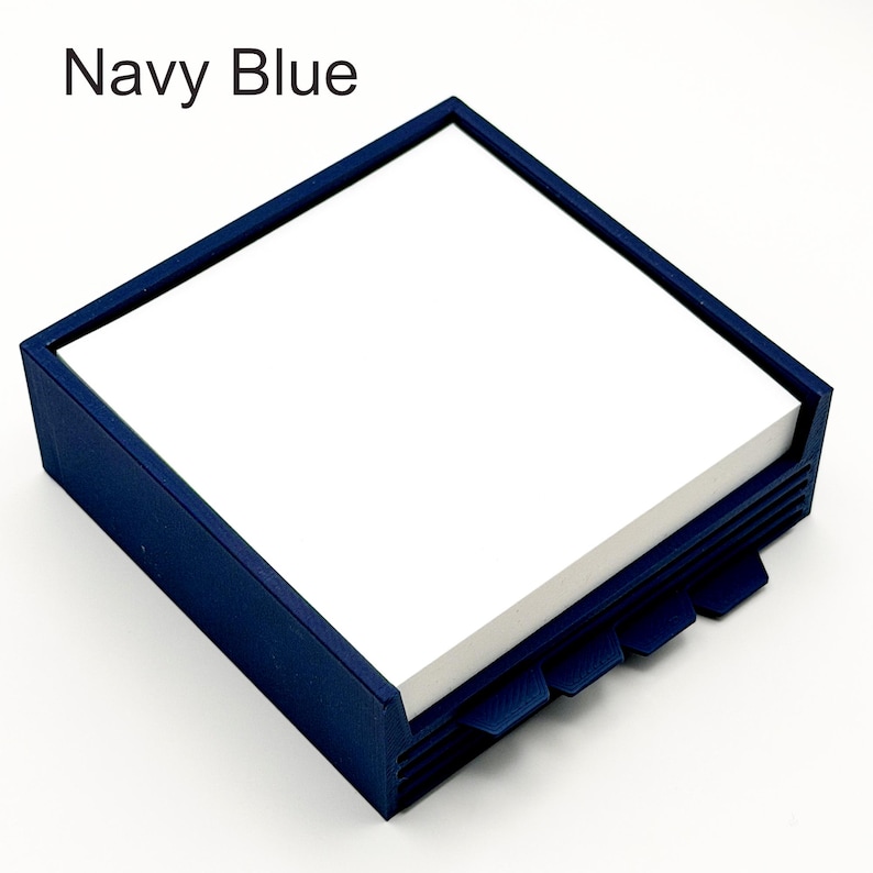 May include: A navy blue square notepad holder with a stack of white notepaper. The holder has a dark blue frame and a series of angled tabs on the bottom edge. The text "Navy Blue" is in the upper left corner.