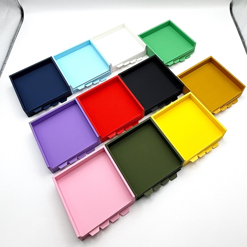 May include: An assortment of colorful square trays in various shades, including navy, light blue, white, green, black, gold, purple, red, yellow, olive green, and pink. Each tray has a square shape with a notched design on the sides.