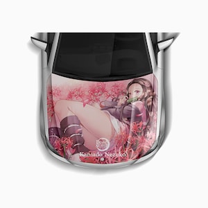 May include: A white car with a pink and red anime character decal on the bonnet. The character is a young woman with long black hair and a pink and white outfit. The decal features the text "Demon Slayer" and "Kamado Nezuko".