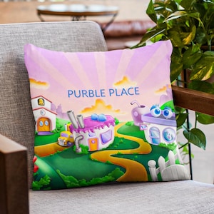 May include: A decorative throw pillow featuring a whimsical cartoon landscape with the text "PURBLE PLACE". The design includes colorful buildings, winding roads, and a vibrant sky in shades of pink and yellow. The pillow is placed on a gray chair.
