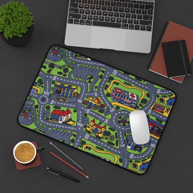 Mousepad featuring the iconic 90s and 2000s city street carpet design, with colorful illustrated roads, buildings, and vehicles. Styled on a black desk with a laptop, coffee cup, notebooks, and pencils.