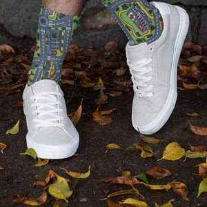 May include: A pair of white sneakers with white laces. The person is wearing socks with a city street pattern in shades of green, blue, and gray.