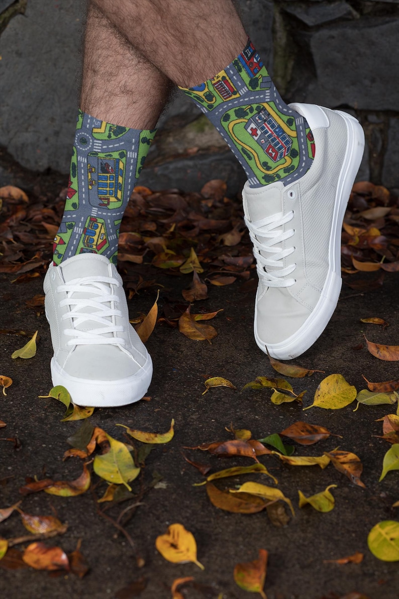 May include: A pair of white sneakers with white laces. The person is wearing socks with a city street pattern in shades of green, blue, and gray.