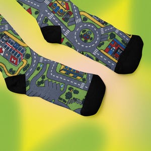 May include: A pair of black socks with a playful design featuring a miniature city with roads, buildings, and trees. The socks are made of a soft, comfortable material and are perfect for adding a touch of whimsy to any outfit.