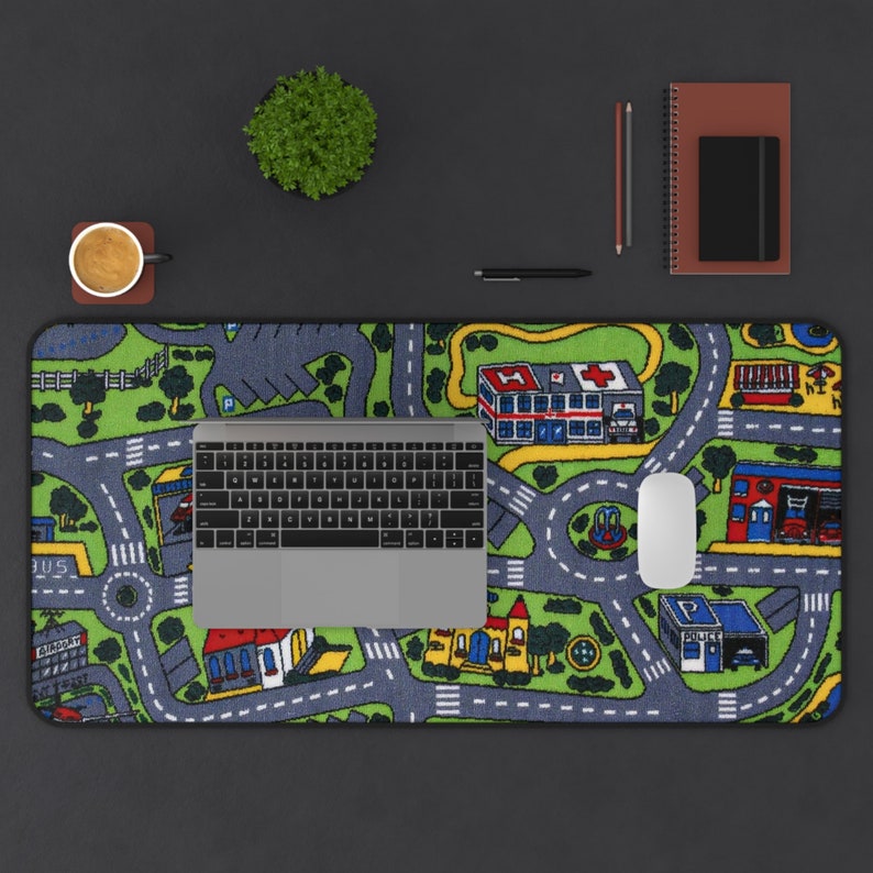 Mousepad featuring the iconic 90s and 2000s city street carpet design, with colorful illustrated roads, buildings, and vehicles. Styled on a black desk with a laptop, coffee cup, notebooks, and pencils.