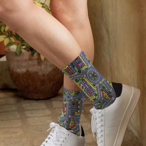 May include: A pair of white sneakers with black trim and a pair of socks with a colorful city street pattern. The socks are worn on a person's feet.