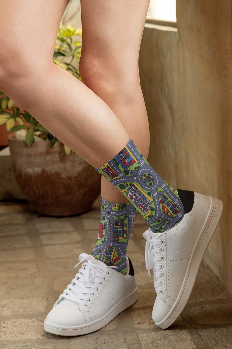 May include: A pair of white sneakers with black trim and a pair of socks with a colorful city street pattern. The socks are worn on a person's feet.