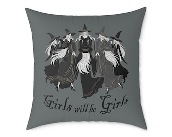 Könnte beinhalten: Quadratisches Kissen mit dunkelgrauem Hintergrund. Das Kissen zeigt eine Grafik von fünf Hexen in schwarzen Kleidern und Hüten mit langen weißen Haaren. Der Text "Girls will be Girls" ist in einer stilisierten Schriftart gedruckt.