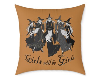 Könnte beinhalten: Quadratisches orangefarbenes Kissen mit einer Grafik von fünf Hexen in schwarzen Kleidern und Hüten mit langen weißen Haaren. Der Text "Girls will be Girls" ist darunter in einer stilisierten Schriftart gedruckt.