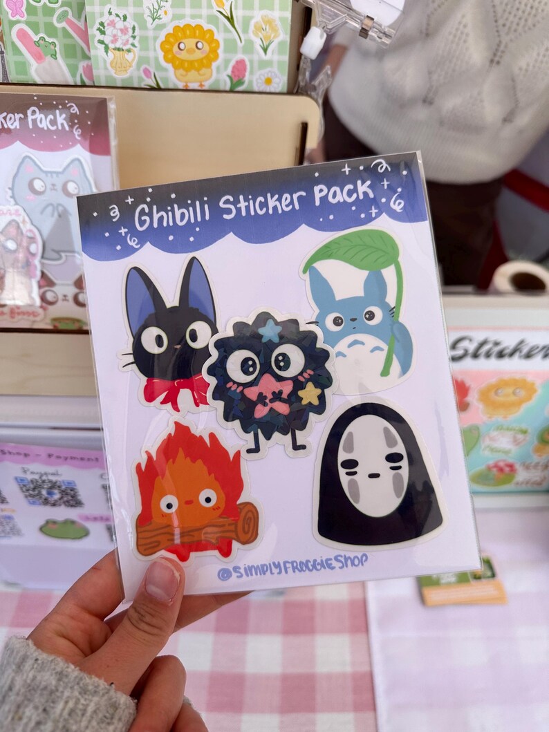 May include: A sticker pack featuring characters from Studio Ghibli films. The pack includes a black cat with a red bow, a black and pink creature with a star, a blue cat with a leaf, a fire spirit, and a No Face character.