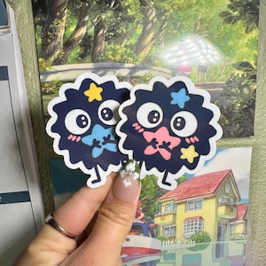 May include: Two black and white fuzzy stickers with cartoon faces, stars, and pink and blue accents. The stickers are on a white background.
