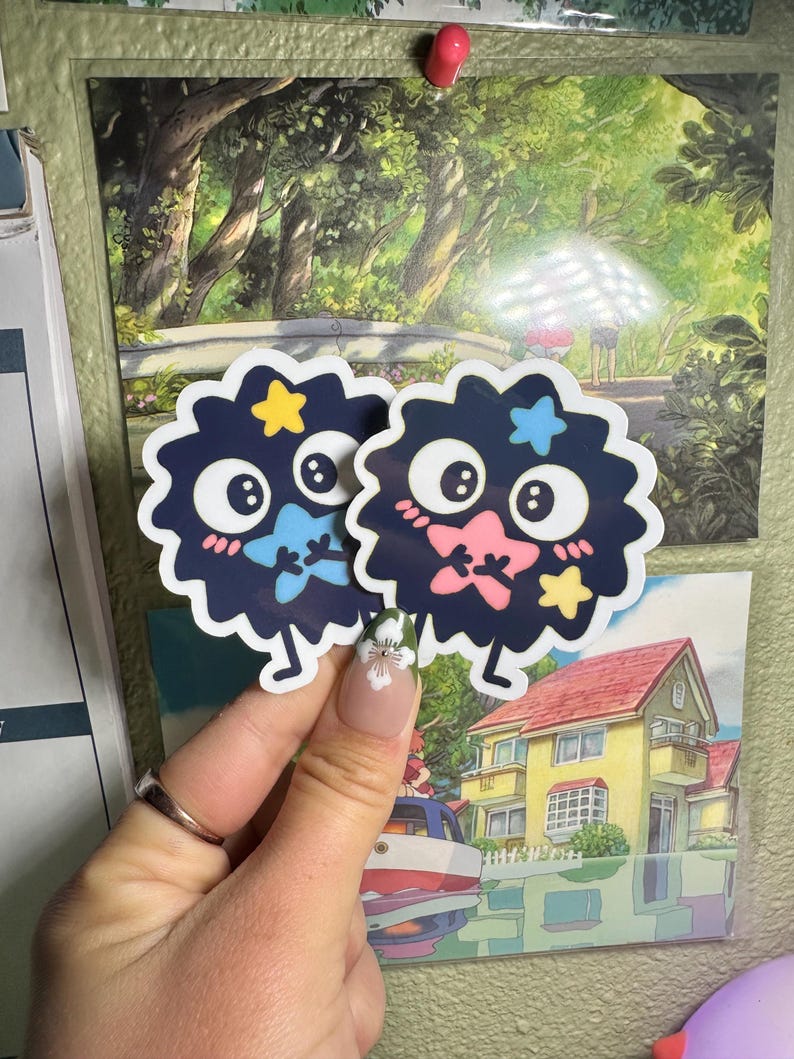 May include: Two black and white fuzzy stickers with cartoon faces, stars, and pink and blue accents. The stickers are on a white background.