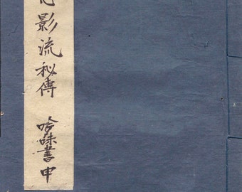 May include: A blue book cover with a white label on the front. The label has black calligraphy that reads "真心 涙 改善  音楽 中".