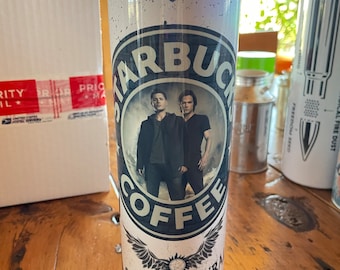 May include: A white stainless steel tumbler with a black and white graphic of two men standing in front of a coffee cup with the words "Starbucks Coffee" and "Supernatural" printed on it.