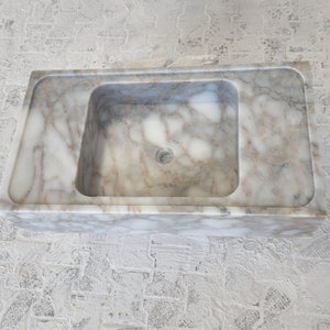 May include: A white marble bathroom sink with a rectangular shape and a square basin. The sink has a smooth, polished surface with subtle gray veining.
