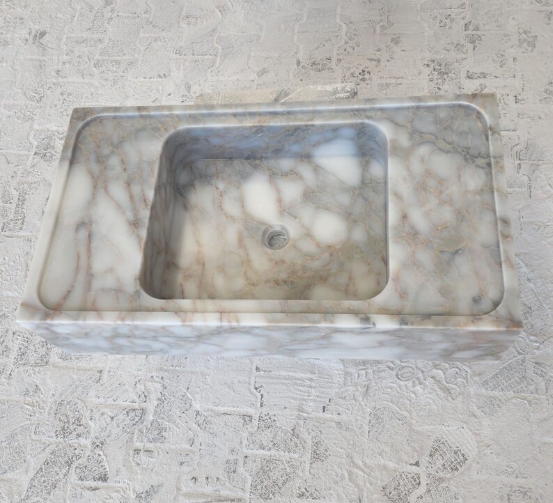 May include: A white marble bathroom sink with a rectangular shape and a square basin. The sink has a smooth, polished surface with subtle gray veining.