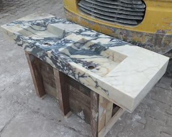 May include: A double sink bathroom vanity countertop made of white marble with black and purple veining. The countertop is supported by a wooden frame.