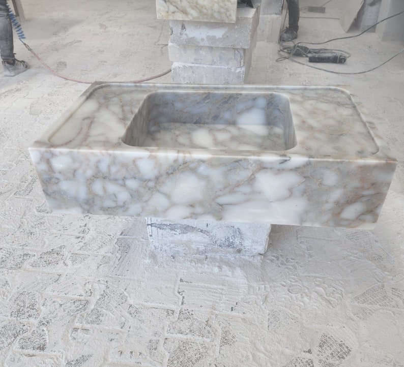 May include: A white marble sink with a rectangular shape and a single basin. The sink is sitting on a concrete base.