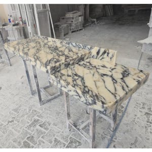 May include: A rectangular stone countertop featuring a cream-colored base with prominent, dark charcoal-colored veining throughout. The surface has a polished finish and includes a raised backsplash edge along the back and one side of the slab.