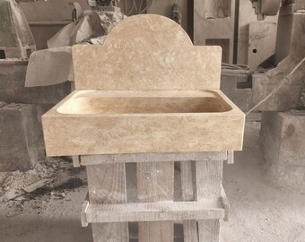 May include: A beige stone sink with a decorative backsplash, sitting on a wooden stand. The sink is made of natural stone and has a rustic look.