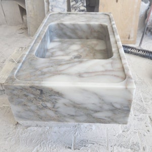May include: A white marble sink with gray veining. The sink is rectangular and has a smooth, polished finish.