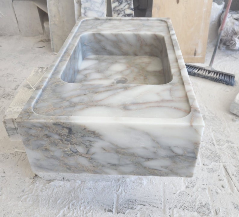 May include: A white marble sink with gray veining. The sink is rectangular and has a smooth, polished finish.