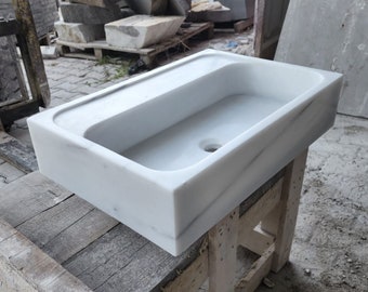 May include: A white marble sink with a rectangular shape and a single drain hole. The sink is sitting on a wooden stand.