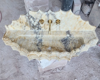 May include: A white marble sink with a scalloped edge and gold taps. The sink is wall-mounted and has a rectangular basin.