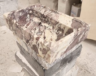 May include: A white marble sink with pink and brown veining. The sink is sitting on a stack of gray and white blocks.